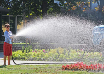 A woman watering a flower bed with a hose. (iStockphoto image)