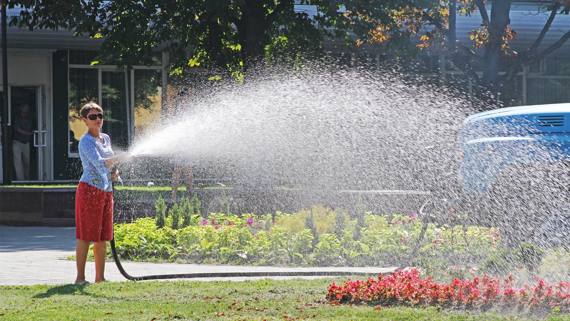 A woman watering a flower bed with a hose. (iStockphoto image)