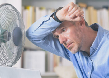 A man sweats due to the heat and tries to cool off by a fan. (iStock image)