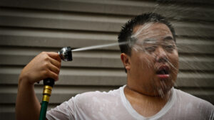 A man seeks relief during a heat wave with a garden hose shower. (Instant Vantage, CC BY-SA 2.0, via Wikimedia Commons)