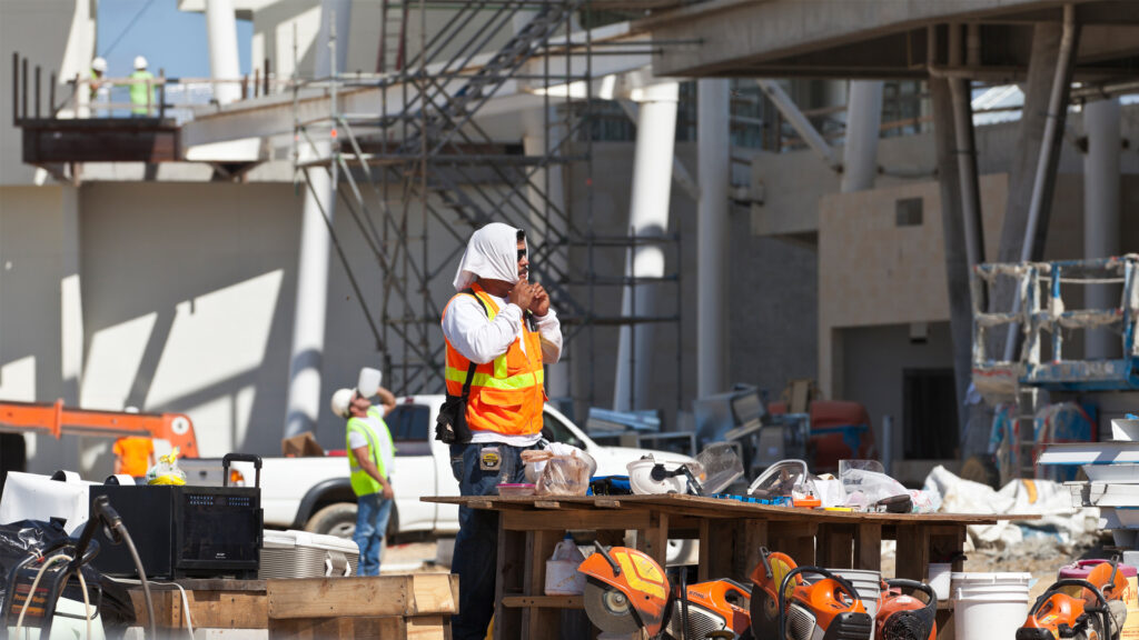 A construction worker ties a towel around his head while another worker can be seen drinking water from a gallon jug on a hot day. (iStock image)