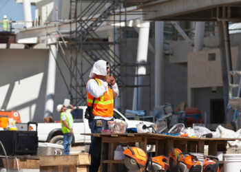 A construction worker ties a towel around his head while another worker can be seen drinking water from a gallon jug on a hot day. (iStock image)