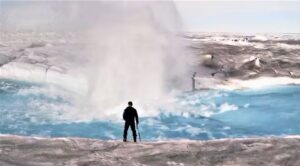 Alun Hubbard stands beside a moulin forming in a meltwater stream on the Greenland ice sheet. (Courtesy of Alun Hubbard)