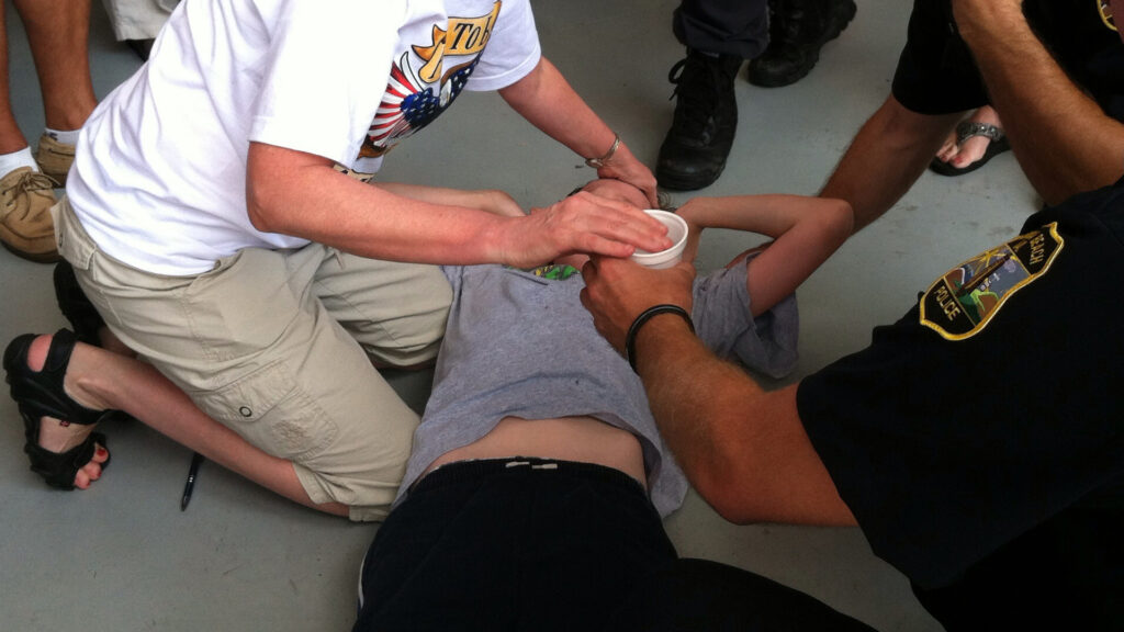 A young man is assisted after passing out from the heat. (Tony Alter, CC BY 2.0, via Flickr)