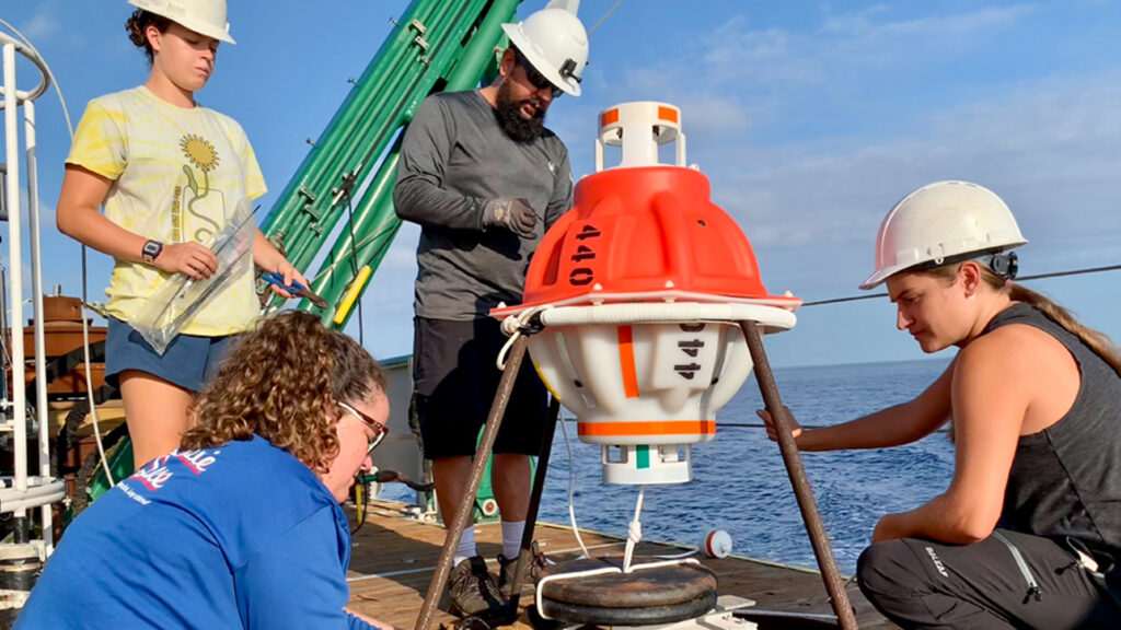 Graduate students Rachel Sampson and Paloma Cartwright, and undergraduate oceanography student Allie Cook, work with mooring technician Eduardo Jardim to prepare a CPIES monitoring device for deployment. (Photo courtesy of Lisa Beal)