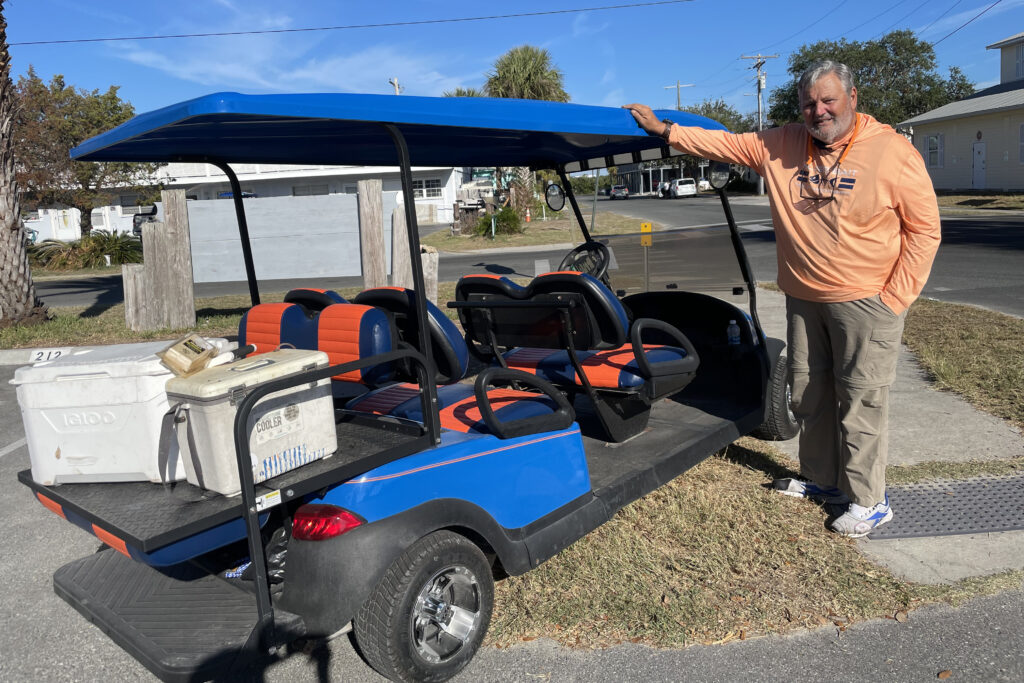 Fred Catfish Abbott played football back in the day at the University of Florida. He gets around Cedar Key on a golf cart that is orange and blue, Gator colors. Between inflation and sky-rocketing housing costs, Cedar Key residents can’t afford to think about COP28, he said. (Amy Green/Inside Climate News)