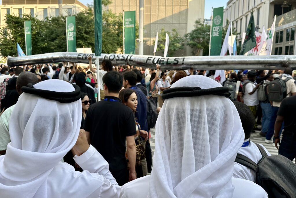 While previous U.N. climate conferences held in democratic European nations generated public rallies attended by hundreds of thousands, the events in UAE this year and Egypt last year permitted no such public engagement. Nevertheless, COP28 Blue Zone attendees organized a protest march that dominated one afternoon of the conference. Along with colorful banners and passionate chants, the activists carried over their heads an oil pipeline in effigy, as if it were being run out of town on a rail. The host oil executives and lobbyists watched, knowing the relative powerlessness of the activists. (Photo by Michal Fidler, text by John Capece)