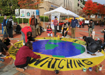 Members of the Sunrise Movement join in painting a mural reminding passers-by that “the earth is watching” before a climate protest in California. (Fabrice Florin, CC-BY-SA 3.0, via flickr)