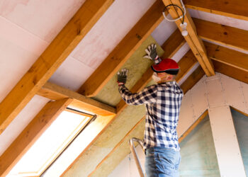 A worker installs insulation in an attic. (iStock image)