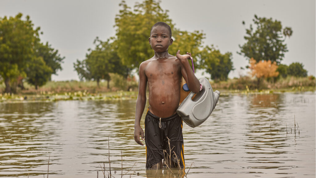 A boy crosses a flooded area, that was a farm before the flood, in Nigeria. (Sadiq Mustapha, CC BY-SA 4.0, via Wikimedia Commons)