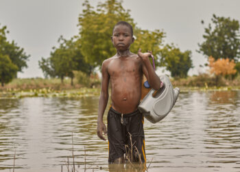 A boy crosses a flooded area, that was a farm before the flood, in Nigeria. (Sadiq Mustapha, CC BY-SA 4.0, via Wikimedia Commons)
