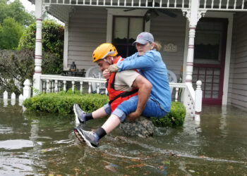 A National Guardsman giving a woman a piggyback in waist-deep floodwaters outside a house as part of rescue operations in flooded areas around Houston in 2017. (Zachary West/National Guard, CC BY 2.0, via Wikimedia Commons)