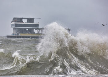 A wave crashing against a seawall on Tampa Bay during a tropical storm with the St Pete Pier in the background. (iStock image)