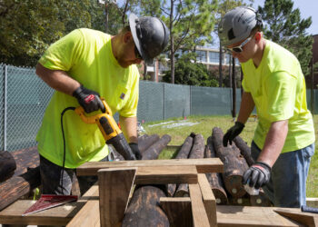 Architect Chris Meyer, left, and an assistant saw logs to the correct length last week. (Photo by Tyler Jones, UF/IFAS)