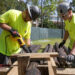 Architect Chris Meyer, left, and an assistant saw logs to the correct length last week. (Photo by Tyler Jones, UF/IFAS)