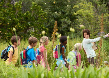 A young teacher with children on a nature field trip. Moving away from the structures and competition of indoor classroom settings matters for students. (iStock image)