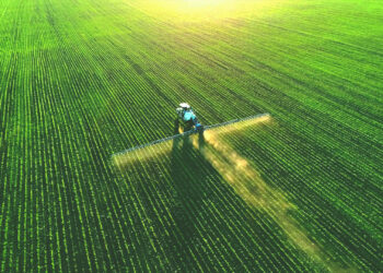 A tractor spreads fertilizer on a field. Fertilizer is a leading source of emissions of nitrous oxide, a planet-warming greenhouse gas. (iStock image)