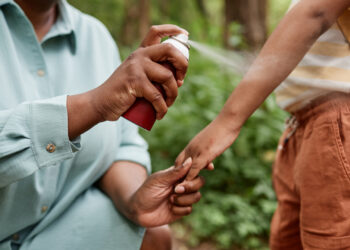 A mother sprays her child with insect repellent. (iStock image)