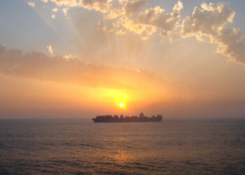 A container ship at sunset (XEON, CC BY 3.0, via Wikimedia Commons)