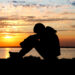 A young person sits by the water at sunset (iStock image)