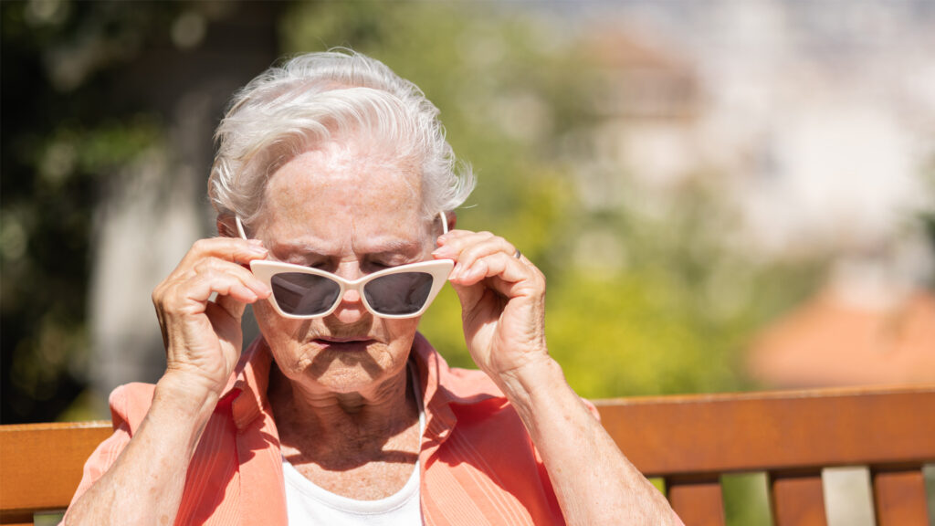 An elderly woman puts on sunglasses on a sunny day (iStock image)