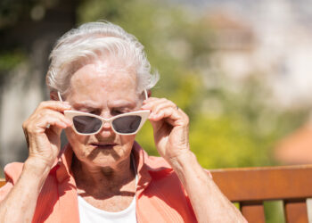 An elderly woman puts on sunglasses on a sunny day (iStock image)