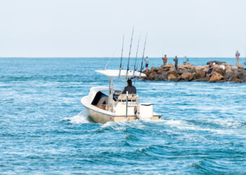 A boat heads out from Venice as people fish from nearby rocks (iStock image)