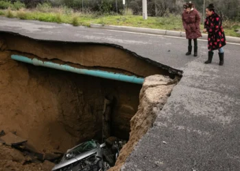 Two passersby peer into a sinkhole that swallowed a section of road in Chatsville, California, during torrential rain on Jan. 10, 2023. (Jason Armond/Los Angeles Times, Getty Images via Grist)