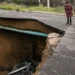 Two passersby peer into a sinkhole that swallowed a section of road in Chatsville, California, during torrential rain on Jan. 10, 2023. (Jason Armond/Los Angeles Times, Getty Images via Grist)