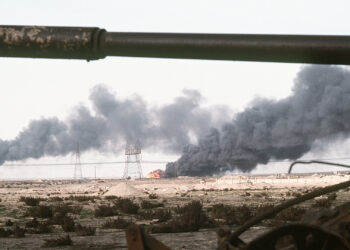 A Kuwaiti oil field set afire by retreating Iraqi troops burns in the distance beyond an abandoned Iraqi tank following Operation Desert Storm. (U.S. Navy; Public domain; via Wikimedia Commons)