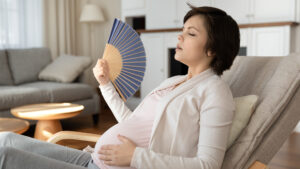 A pregnant woman cools herself with a fan (iStock image)