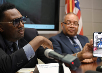 Imola Automotive USA CEO Rodney Henry, left, plays a video of himself inside an electric SUV during a Sept. 2 press conference. Henry said that the company aims to break ground on an electric vehicle plant in Fort Valley, Georgia in the next nine to 12 months. (Katie Tucker/Macon Telegraph)