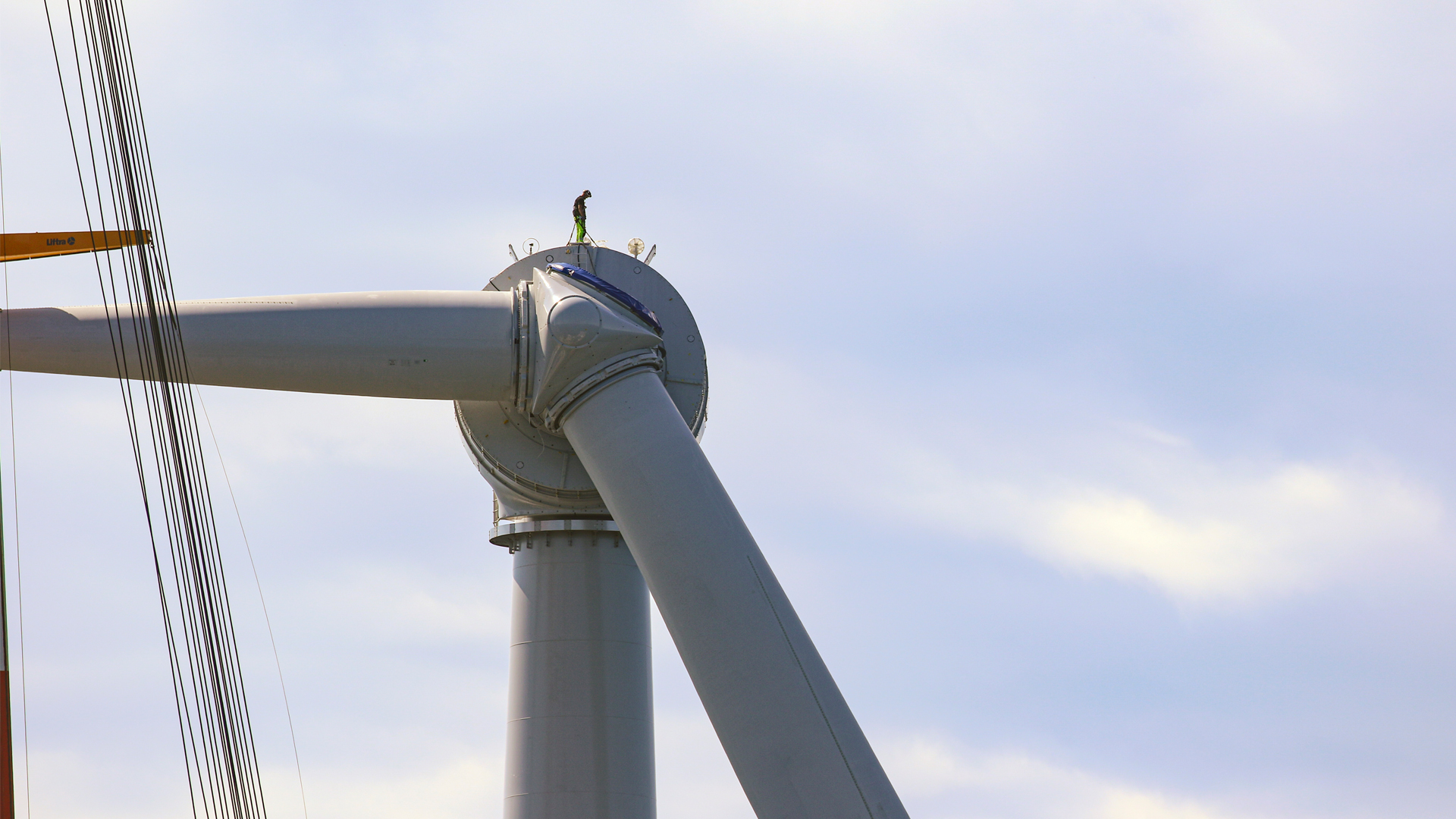 A worker stands on a wind turbine being constructed off the coast of Rhode Island. (BOEM-OPA, CC BY-SA 2.0, via Wikimedia Commons)