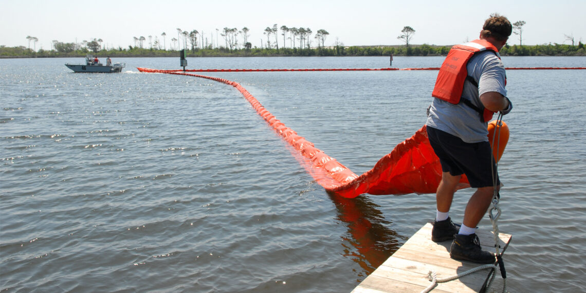 Members of the Naval Air Station Pensacola Pollution Response unit deploy an oil containment boom to protect environmentally sensitive grass beds from the Deepwater Horizon oil spill in 2010. (U.S. Navy photo by Patrick Nichols, Public domain, via Wikimedia Commons)
