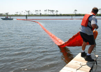 Members of the Naval Air Station Pensacola Pollution Response unit deploy an oil containment boom to protect environmentally sensitive grass beds from the Deepwater Horizon oil spill in 2010. (U.S. Navy photo by Patrick Nichols, Public domain, via Wikimedia Commons)