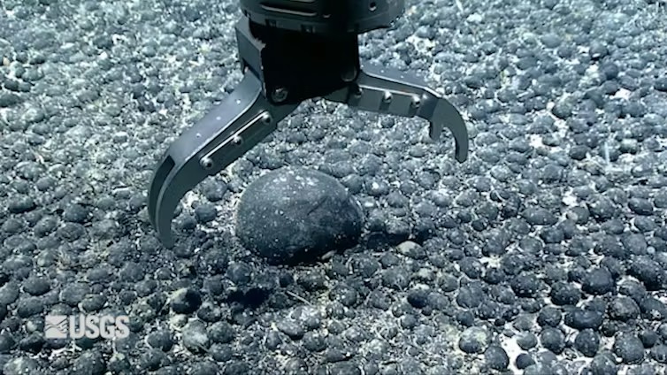 A metal claw reaches for an iron and manganese nodule on the seabed for testing. (USGS Pacific Coastal and Marine Science Center)