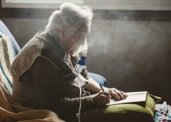 An older adult writes while using a machine with a face mask that assists with breathing. Many older adults rely on electric-powered medical equipment, such as portable oxygen and nebulizers that help them breathe. (Westend61 via Getty Images)