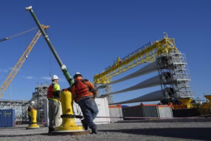 Workers in New London, Conn., prepare a generator and its blades for transport to South Fork Wind’s offshore wind farm in 2023. To build an offshore wind farm requires manufacturing jobs, parts suppliers, dockworkers, crane operators, ship crews, as well as the wind farm construction crews and maintenance teams and many more businesses and their employees. (AP Photo/Seth Wenig)